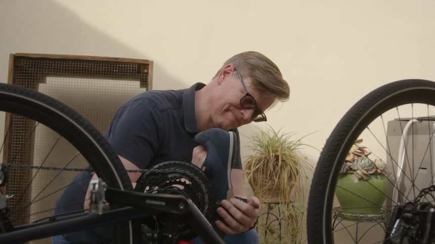 A man attaches a shoe to the pedal of a bicycle in the backyard