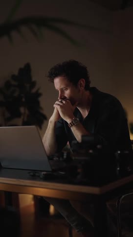 Vertical video of a tired man working on a laptop in his home office at night