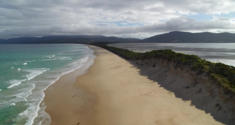 Moving along south american coast with light waves coming in sandy beach green water and overcast mountain range in the background