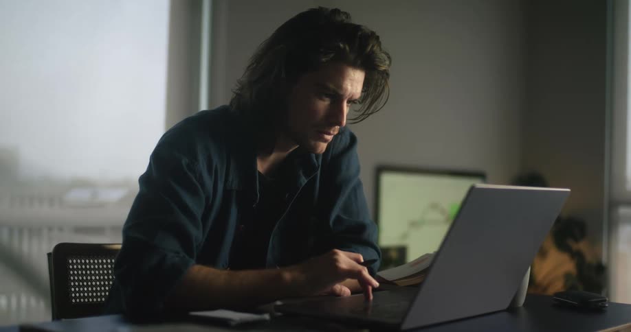 A man is typing on his laptop and writing things down