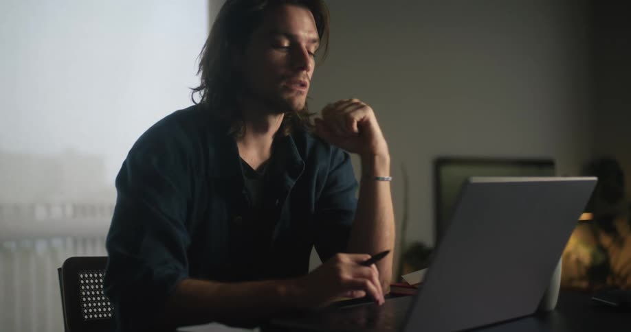 Man sitting at desk working on laptop while alternately writing notes