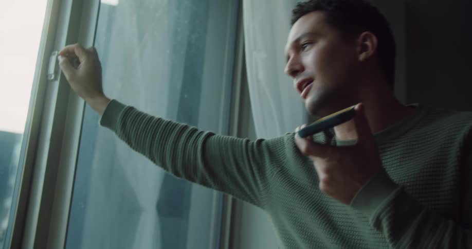 A man stands in front of a large window while conversing via his smart phone