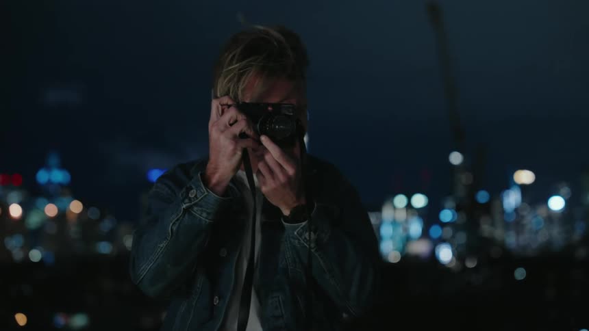 Blonde photographer takes pictures with a camera at night in front of the city skyline