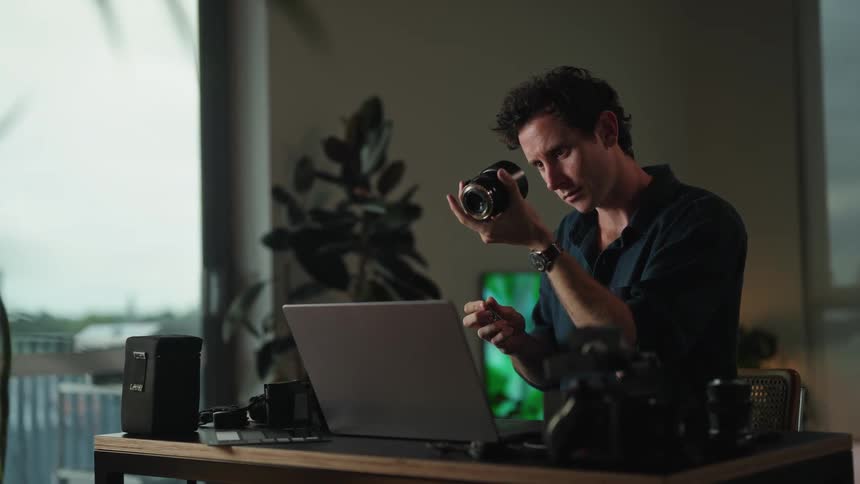 A man is looking at his camera lens at the desk