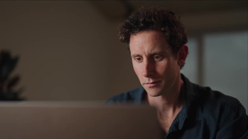 A man sitting looking at a camera lens and then looking into the distance and smirking