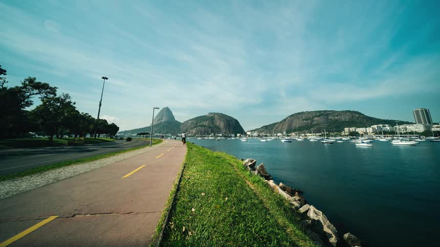 A time lapse of a lake with boats in it next to a road with cars and poeple walking