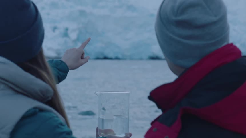 A person points to a beaker and then to an icy mountain