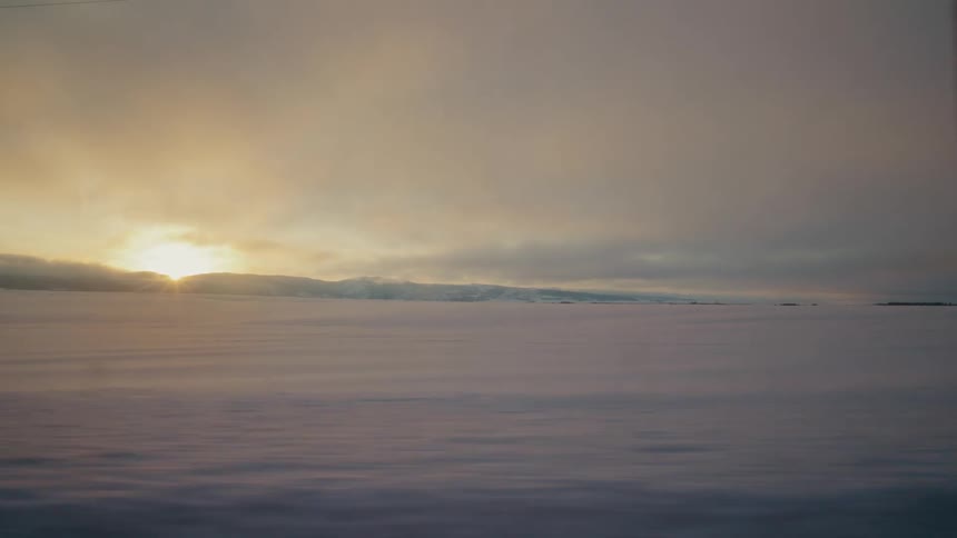Sun rises over mountain to shine across snow covered countryside near building