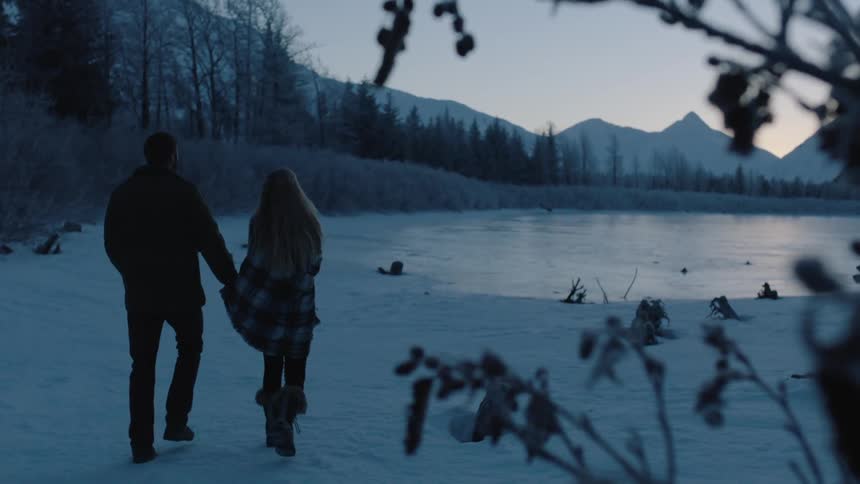 A man and woman walk toward a snowy pond