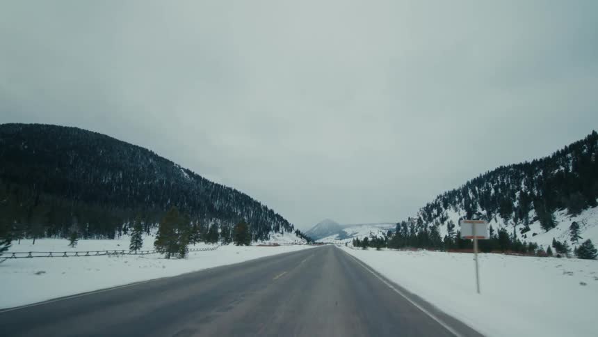 A highway runs past snow covered trees on a hill