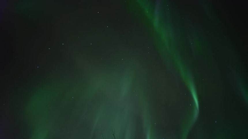 The glowing green light of the aurora borealis moves across a star filled night sky