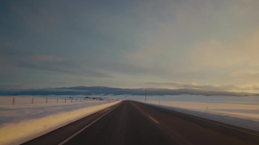 A rural highway runs through snow blanketed fields