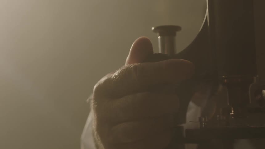 A hand turns a knob on a microscope