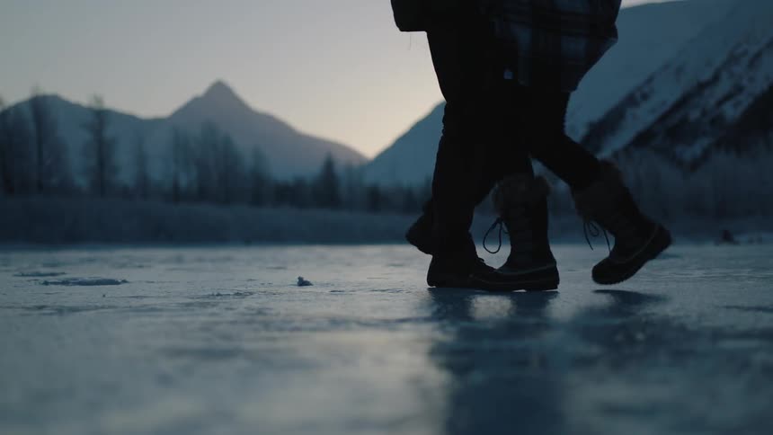 A man and woman walk on an icy pond