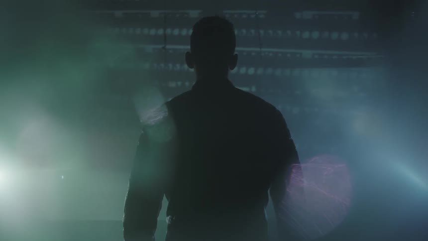 A man stands watching a projection on the wall