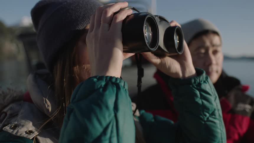 A woman holds binoculars to her face on a boat