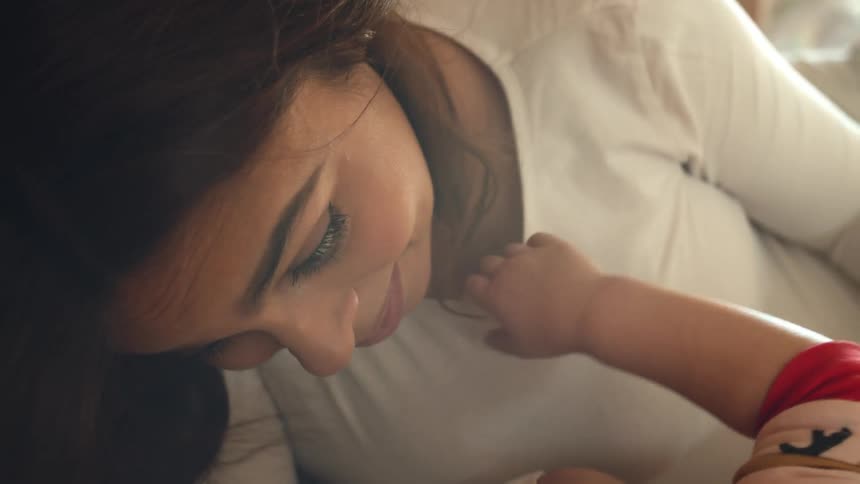 A close up of a womans face as a child outs their hand and arm around her neck as she smiles