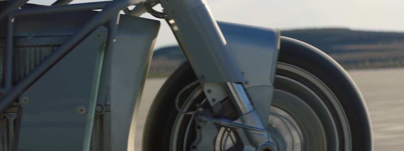 A motorcycle travels across the desert and there are mountains in the distance
