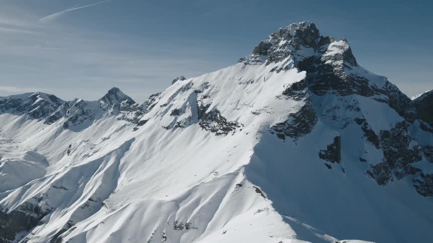 A snowy mountain range with high peaks against a blue sky