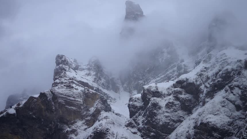 Snow falls onto craggy mountain obscured by low lying cloud