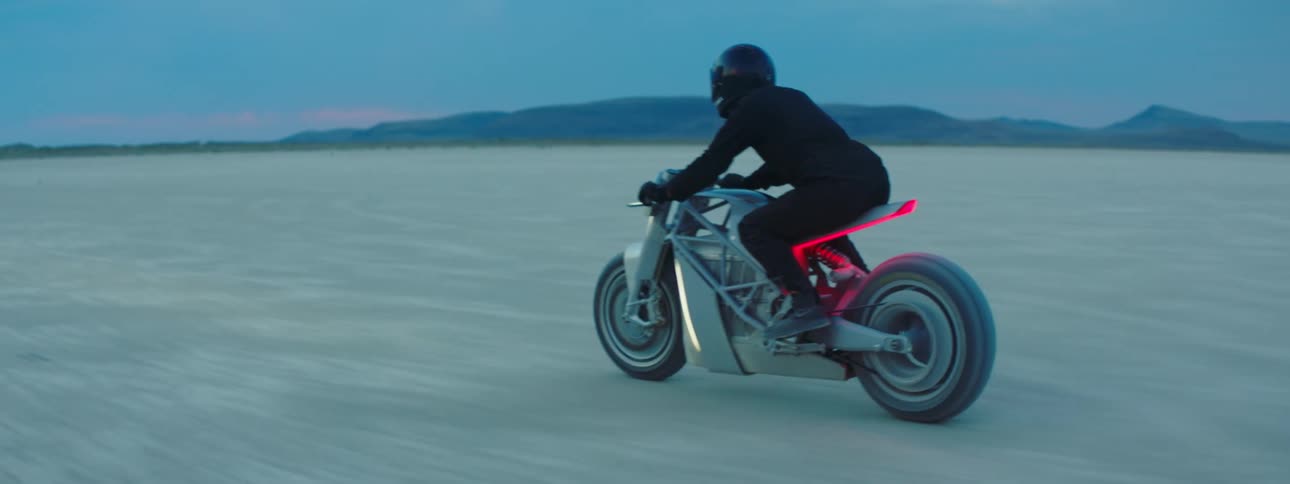 A person riding a motorcycle across a desert landscape at sunset