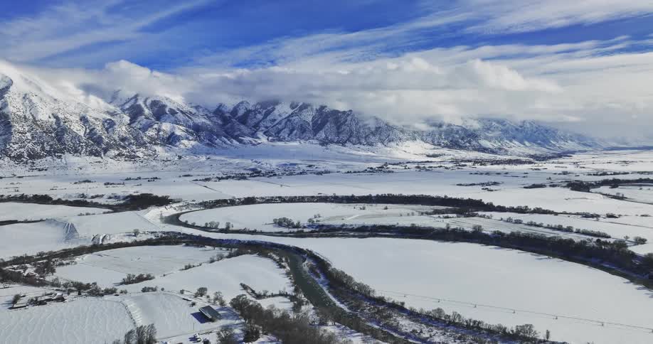 An aerial landscape view of a snow covered rural area with snow covered mountain ranges in the background