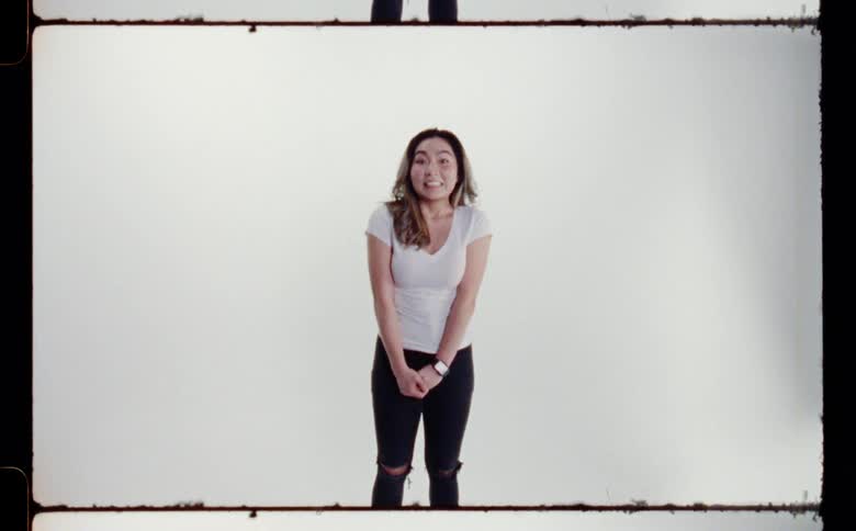 Woman with white t shirt and ripped black jeans poses and smiles at camera in the studio