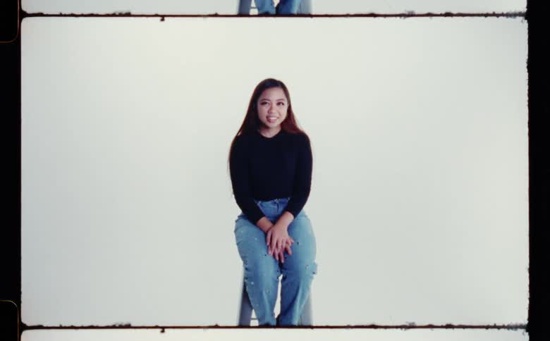 A young woman smiles while posing on a stool