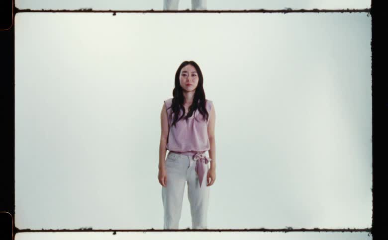 Woman with wavy hair pink blouse and white pants poses for the camera in the studio