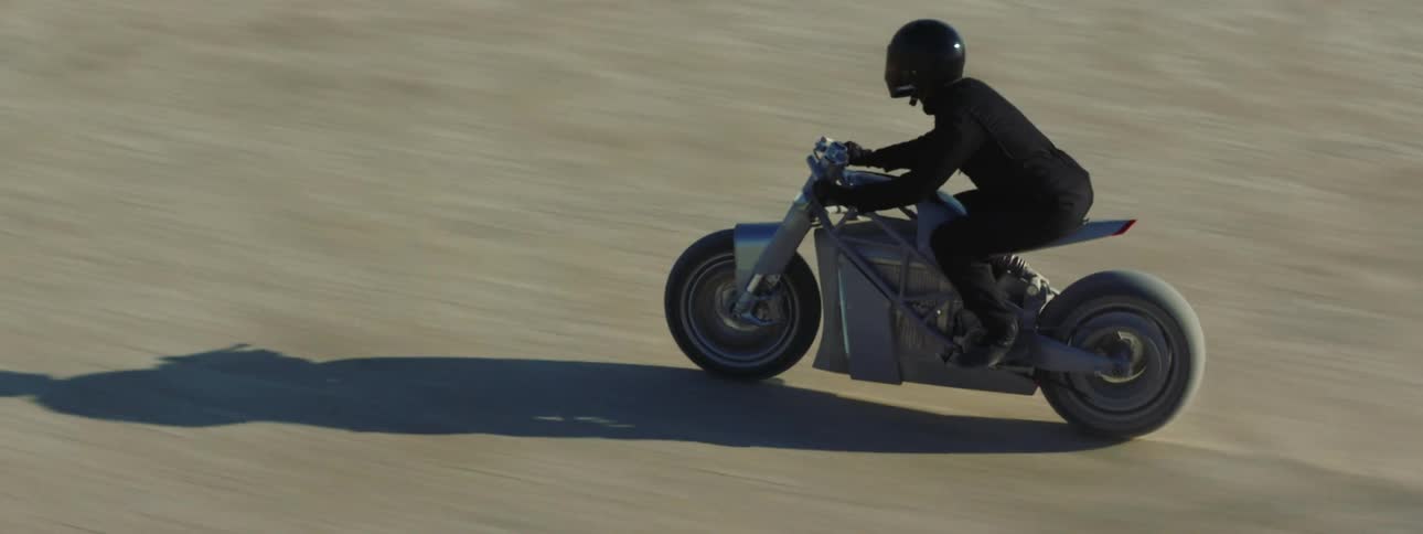 Casting shadow ahead of the motorcycle a motorcyclist rides across sand