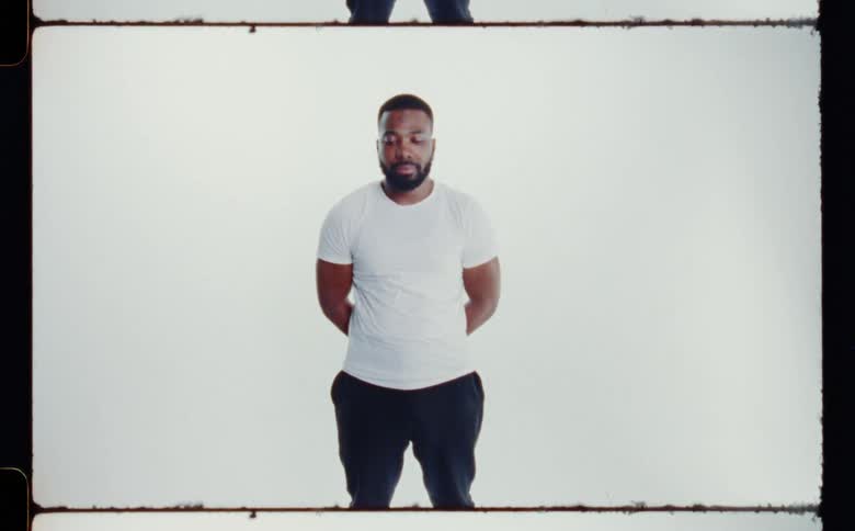 Man with beard white t shirt and black pants poses for the camera in front of white screen backdrop in photography studio