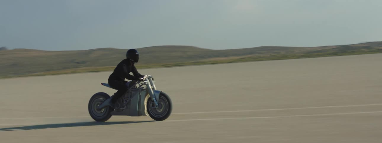 A rider wearing a helmet and all black traveling on a motorcycle over packed sand in a desert