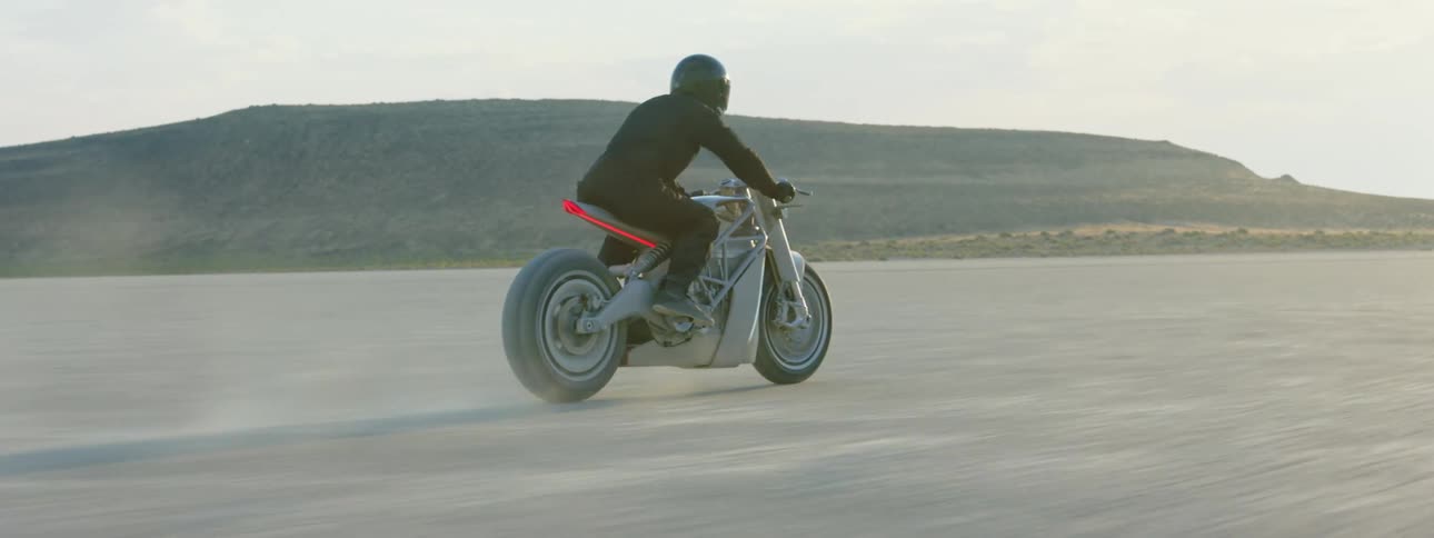 Motorcyclist rides across plain with mountain in background