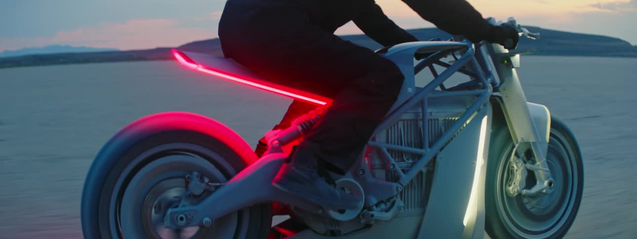 Biker with black helmet jacket and pants rides silver motorcycle in the desert at dusk