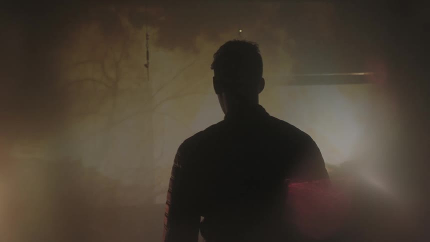 A man stands watching as fires go on in front of him