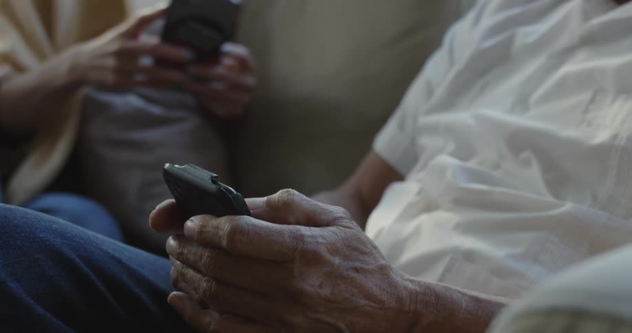 A man and woman sitting on a couch together while each are on their smartphones texting and scrolling