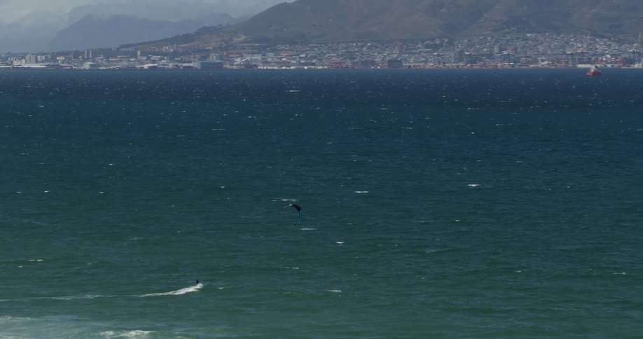 A person is kitesurfing across the open ocean with a city in the background