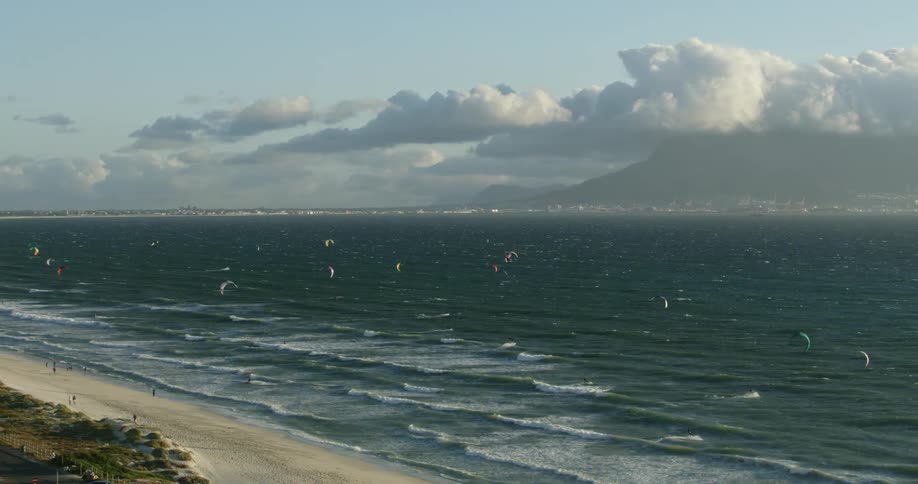Aerial view of kiteboarders kitesurfing across the waves and ocean water near a white sand beach