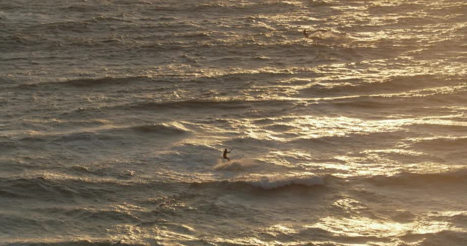 Two people kitesurfing across waves in teh open ocean at sunset