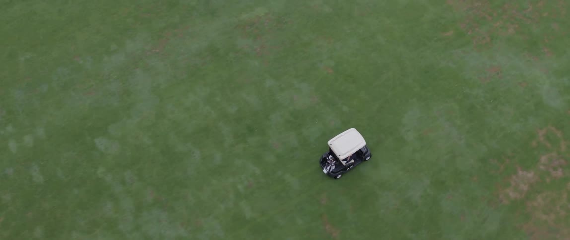 Golfer drives golf cart across golf green