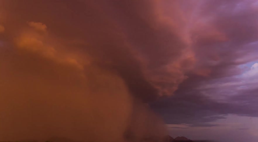 A purple and orange tinted dust storm rolling over desert field with traffic driving by on the road