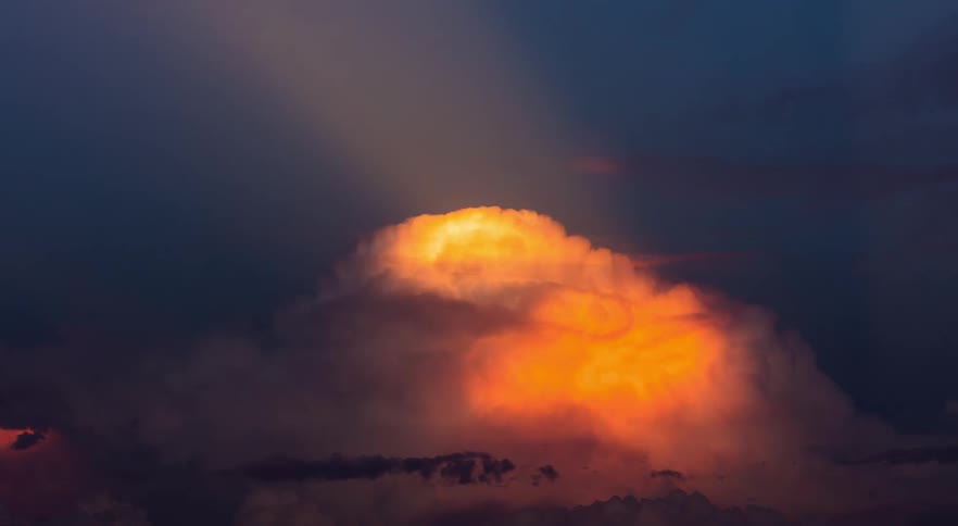 Thunderstorm cloud top lit up by the sun with red and orange colors