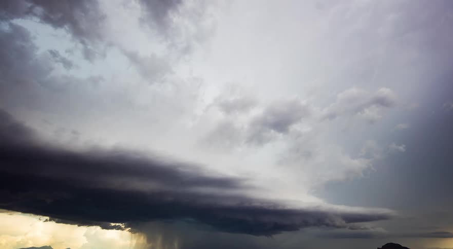 Wide landscape of horizon city lights in valley with dark clouds and storm coming in