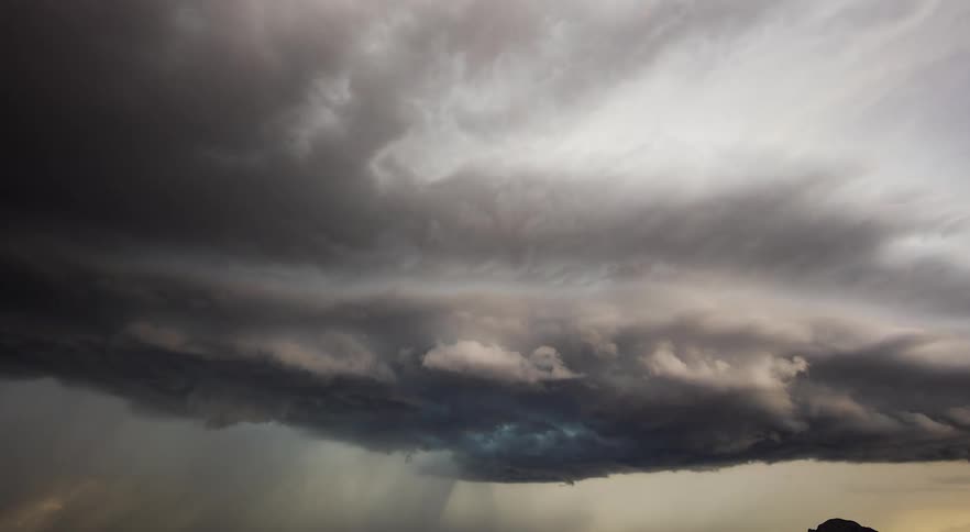 A big dark shelf cloud moves over a town during a storm
