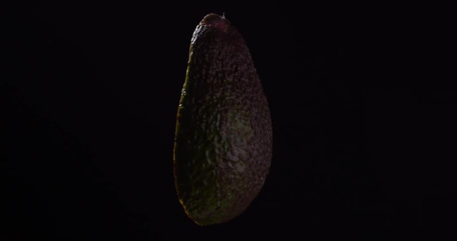 Light shines on half of an organic avocado with the pit in the middle as it rotates in the darkness while being prepared for guacamole
