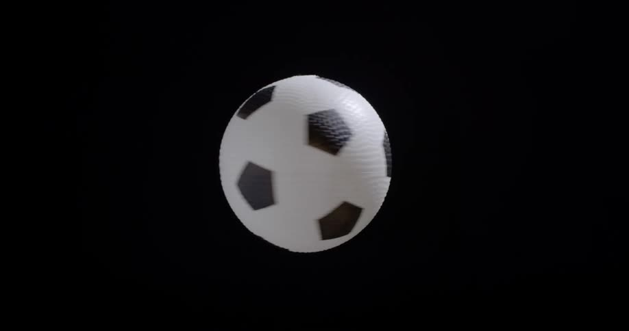 Light shines on a black and white soccer ball as it rotates in the darkness while flying through the air on its way to the goal