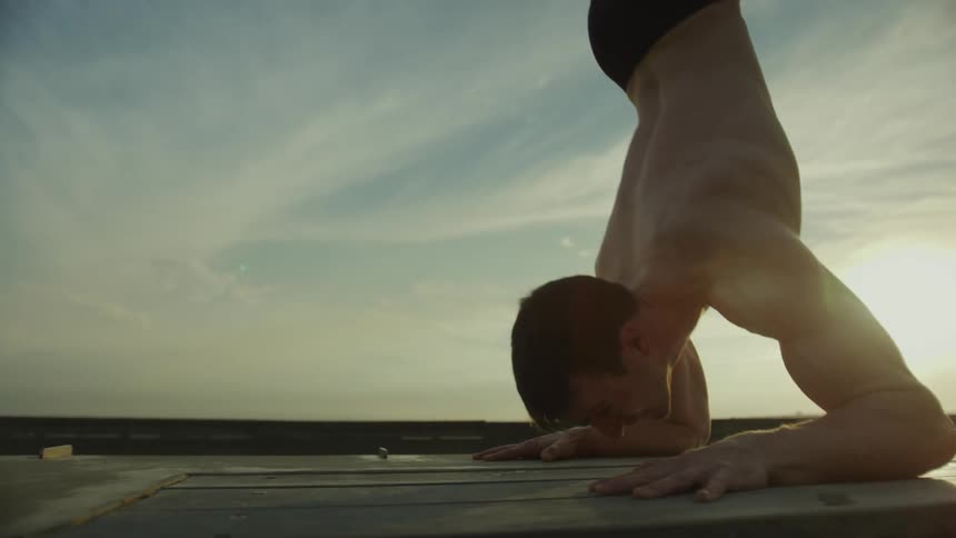 Topless man with black pants performs calisthenics exercise outdoors at sunset