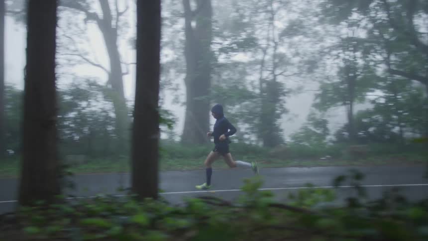 Man with raincoat shorts socks and white shoes run along highway in the forest in fog