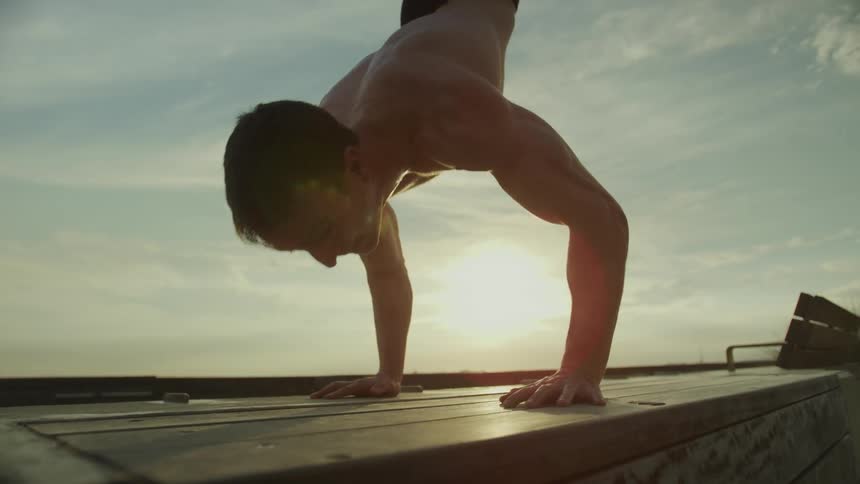Close up of a young strong muscular shirtless man standing on hands at sunset