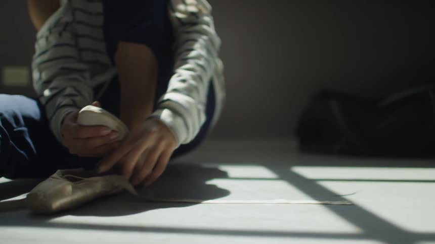 A person sits on the floor and puts on their ballet slipper